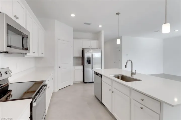 Kitchen with a sink, stainless steel appliances, light countertops, and decorative light fixtures