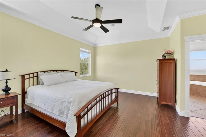 Bedroom featuring ornamental molding, dark wood-type flooring, a ceiling fan, and a tray ceiling