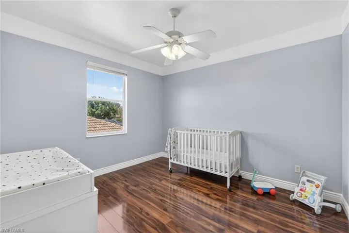 Bedroom with dark wood-style flooring, a nursery area, and ceiling fan