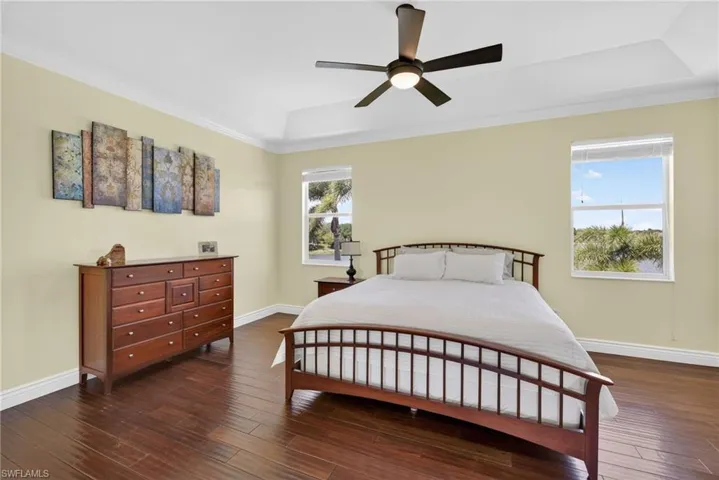 Bedroom with a raised ceiling, dark wood finished floors, a ceiling fan, and ornamental molding