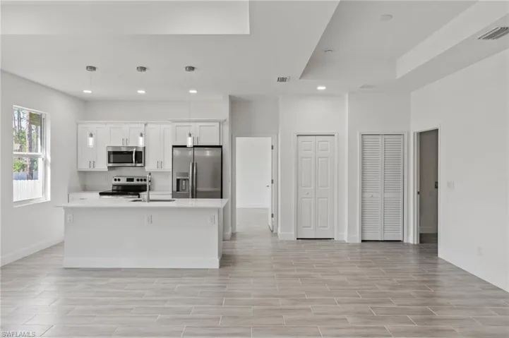 Kitchen featuring stainless steel appliances, white cabinets, sink, pendant lighting, and a kitchen island with sink