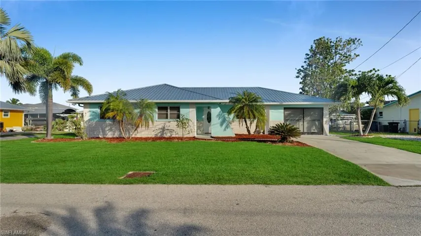 Ranch-style house featuring a metal roof, a front lawn, concrete driveway, and brick siding