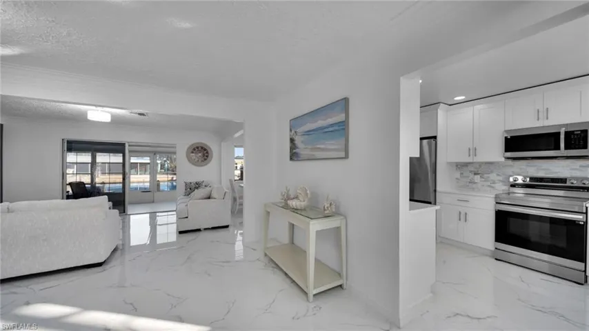 Kitchen with a textured ceiling, stainless steel appliances, light marble finish floors, open floor plan, and white cabinetry