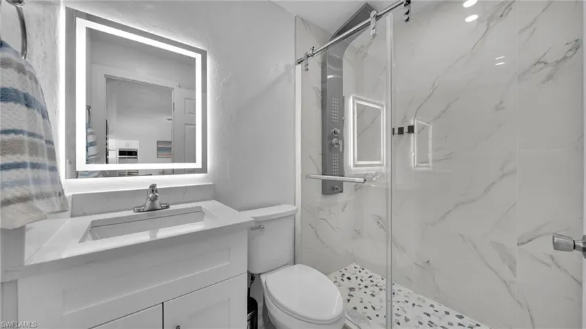 Bathroom with a textured wall, a marble finish shower, and vanity