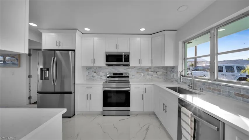 Kitchen featuring light marble finish flooring, appliances with stainless steel finishes, backsplash, light stone counters, and white cabinetry