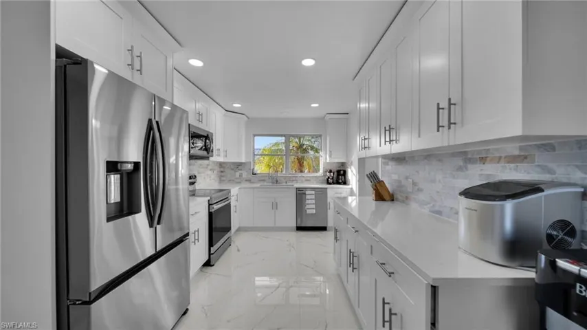 Kitchen featuring appliances with stainless steel finishes, light marble finish flooring, backsplash, white cabinetry, and recessed lighting
