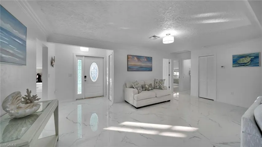 Foyer entrance with ornamental molding, light marble finish floors, and a textured ceiling