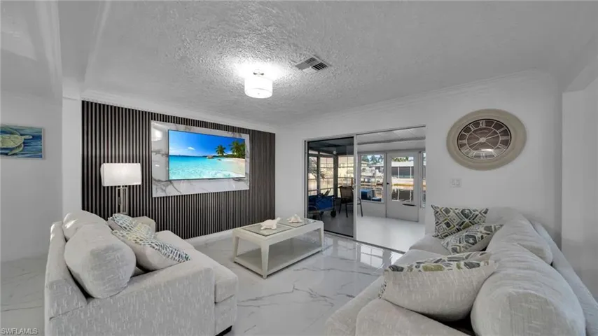 Living room with marble tiled floors, crown molding, a textured ceiling, and an accent wall