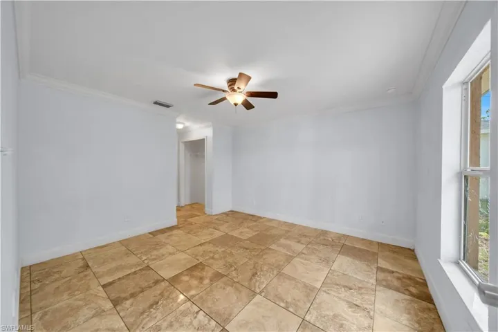 Spacious room featuring neutral-toned tile flooring, white baseboards, and crown molding