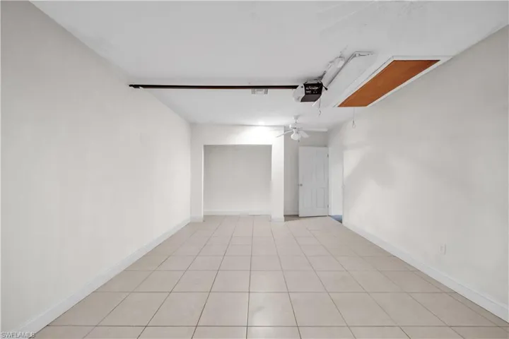 Spacious room featuring neutral-toned tile flooring, white painted walls, and a white ceiling fan
