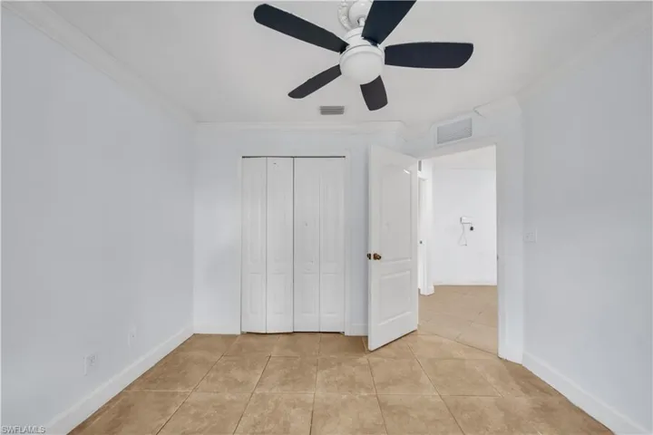 Room featuring neutral tile flooring, white walls, bi-fold closet doors, crown molding, and a ceiling fan with light