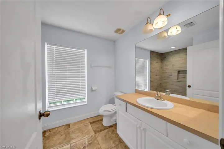 Bathroom featuring a white vanity with a light wood-finish countertop and an integrated sink, a large wall-mounted mirror, and a three-light fixture