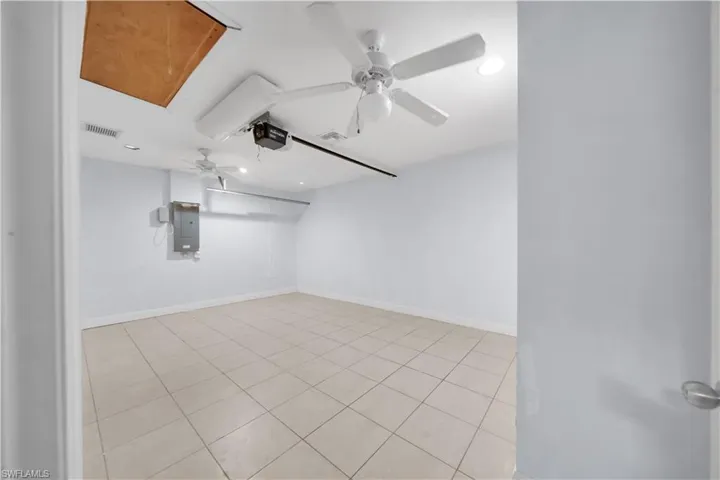 Spacious room featuring light-toned tile flooring, white walls, two ceiling fans, recessed lighting, and a utility panel