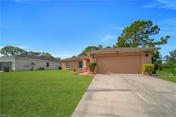 Single-story stucco residence featuring an attached garage with a concrete driveway, mature landscaping, and an expansive lawn