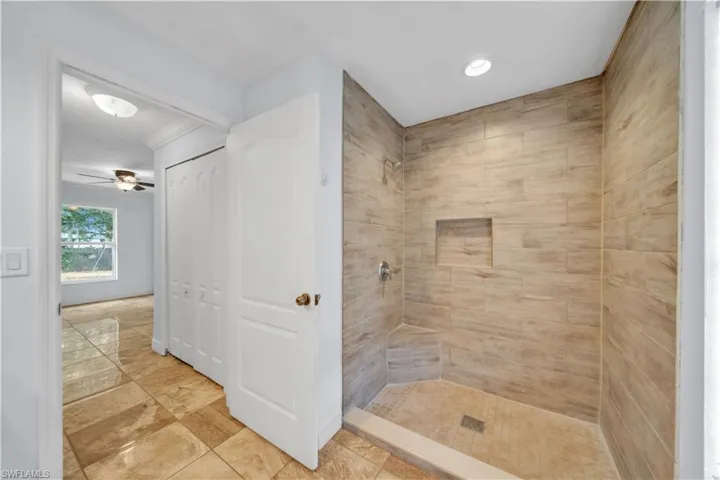 Walk-in shower featuring light wood-finish wall tiling, a built-in bench, a recessed niche, a rain shower head, and a chrome-finish handheld shower fixture