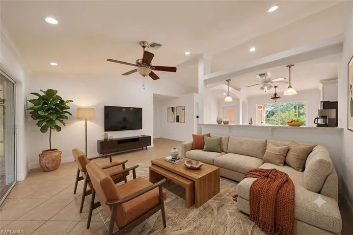 Spacious living area featuring vaulted ceilings, recessed lighting, tile flooring, a ceiling fan, and a pass-through opening to an additional room