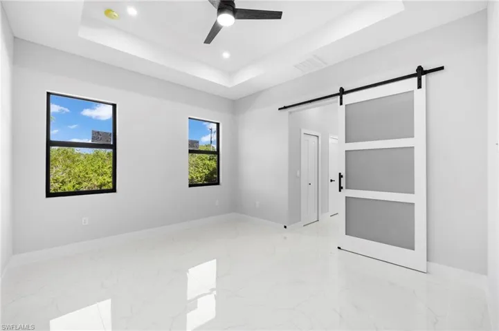 Empty room featuring a barn door, a tray ceiling, ceiling fan, and light tile floors