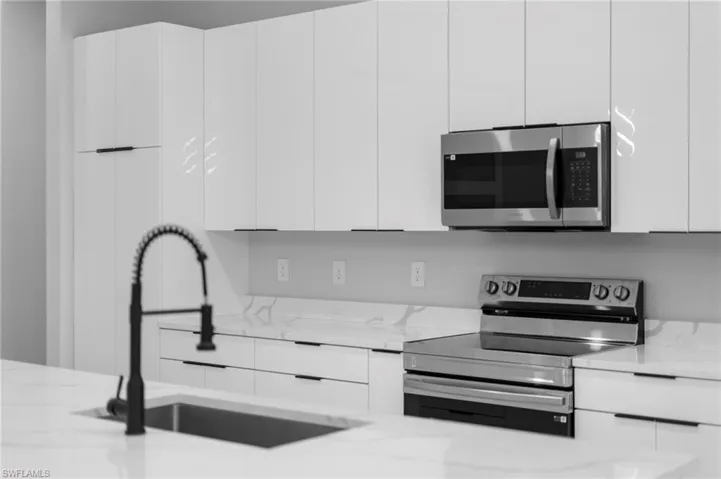 Kitchen featuring light stone counters, sink, white cabinets, and appliances with stainless steel finishes