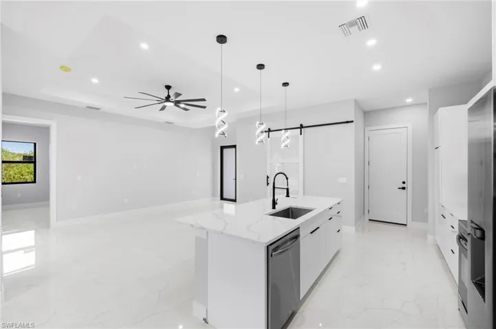 Kitchen with white cabinets, a kitchen island with sink, a barn door, sink, and ceiling fan