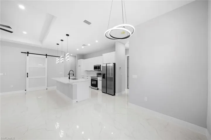 Kitchen featuring stainless steel appliances, a barn door, white cabinets, light tile floors, and pendant lighting