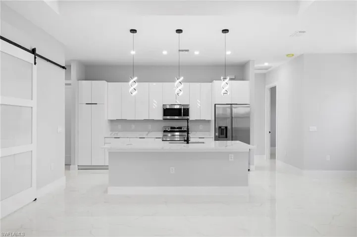 Kitchen with decorative light fixtures, a center island with sink, a barn door, appliances with stainless steel finishes, and light tile floors