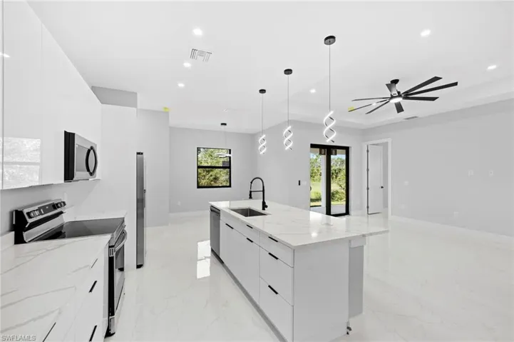 Kitchen featuring decorative light fixtures, ceiling fan, white cabinetry, an island with sink, and appliances with stainless steel finishes