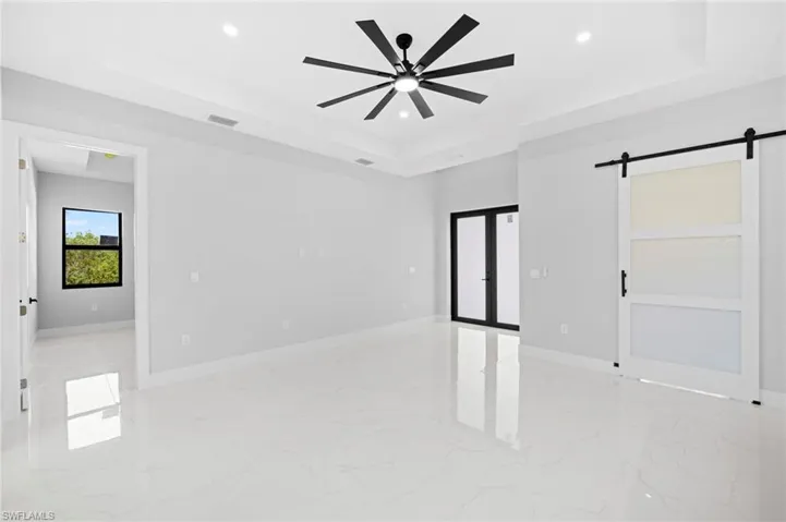 Spare room with ceiling fan, a barn door, light tile flooring, and a raised ceiling