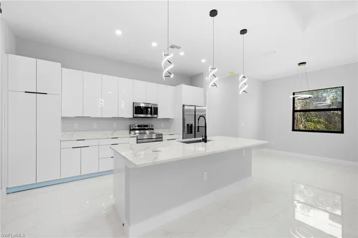 Kitchen with decorative light fixtures, light tile flooring, a spacious island, appliances with stainless steel finishes, and sink