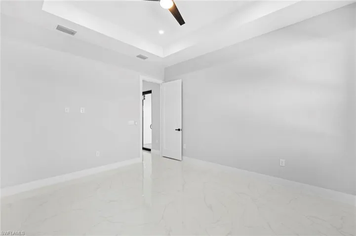 Tiled empty room with ceiling fan and a tray ceiling
