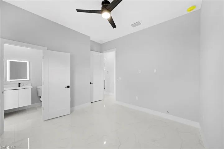 Unfurnished bedroom featuring ceiling fan, ensuite bathroom, and light tile flooring