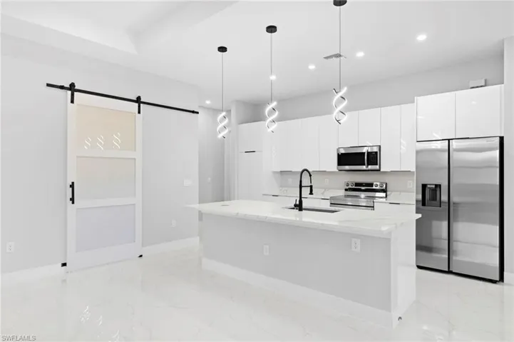 Kitchen with stainless steel appliances, hanging light fixtures, a kitchen island with sink, a barn door, and sink