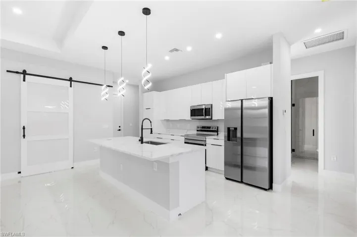 Kitchen with stainless steel appliances, an island with sink, decorative light fixtures, a barn door, and sink