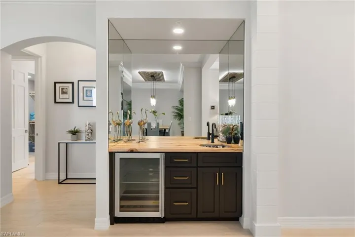 Bar with sink, wood counters, wine cooler, light hardwood / wood-style floors, and decorative light fixtures