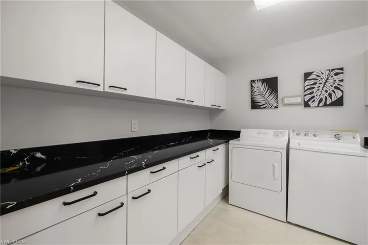 Clothes washing area with cabinets, light wood-type flooring, and washer and clothes dryer