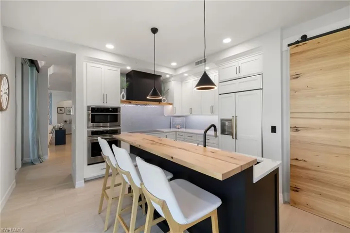 Kitchen with butcher block counters, hanging light fixtures, a barn door, ventilation hood, and white cabinets