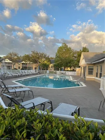 Community pool and hot tub featuring a patio lounge area overlooking lake with clubhouse adjacent