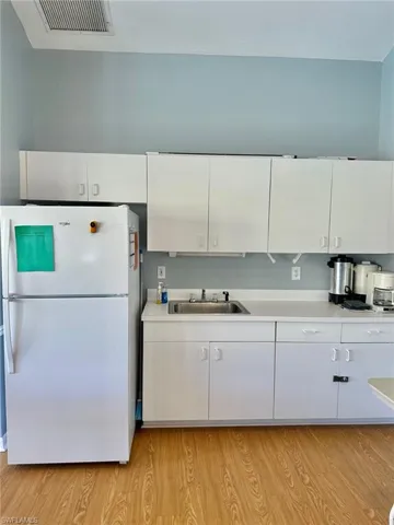 Community Clubhouse with freestanding refrigerator, light countertops, white cabinetry, and light wood-style flooring