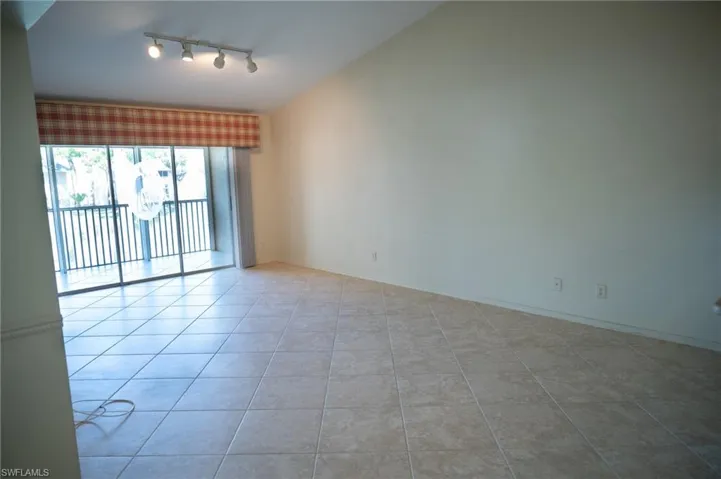 Unfurnished room with track lighting, etched design sliding glass doors, lofted ceiling, and light tile patterned floors