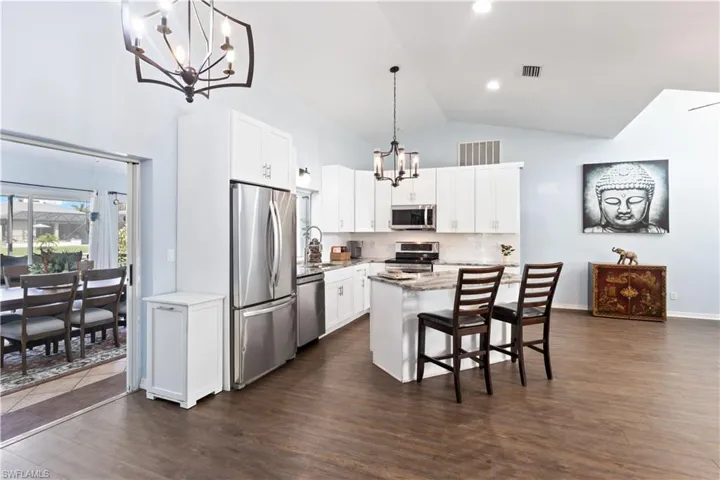Kitchen with hanging light fixtures, appliances with stainless steel finishes, a kitchen island, and white cabinets