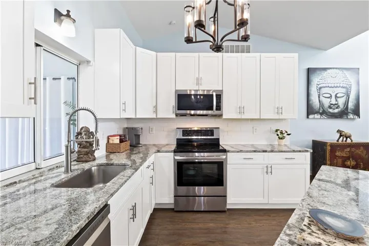 Kitchen with lofted ceiling, dark hardwood / wood-style floors, sink, white cabinetry, and appliances with stainless steel finishes