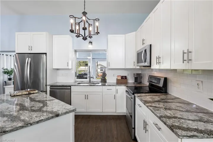Kitchen featuring dark stone countertops, sink, white cabinets, decorative light fixtures, and appliances with stainless steel finishes