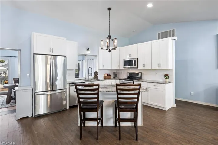 Kitchen featuring lofted ceiling, stainless steel appliances, a center island, decorative light fixtures, and dark hardwood / wood-style flooring