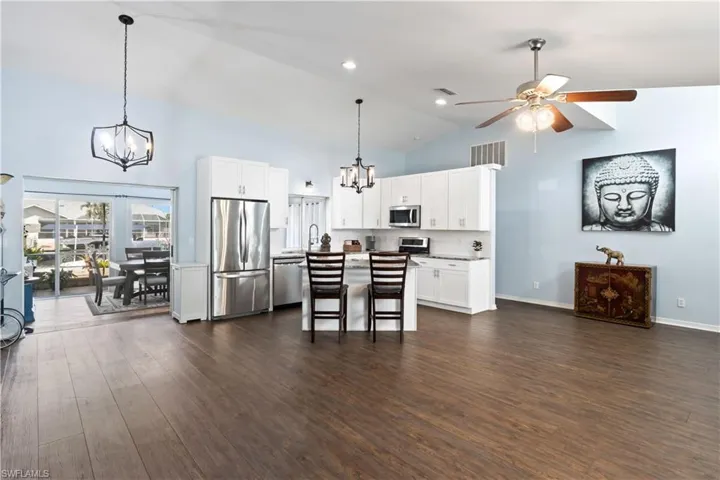 Kitchen with white cabinets, a kitchen island, appliances with stainless steel finishes, a breakfast bar area, and dark wood-type flooring