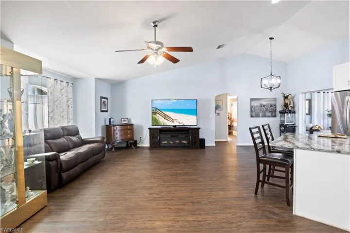 Living room with ceiling fan with notable chandelier, lofted ceiling, and dark hardwood / wood-style floors
