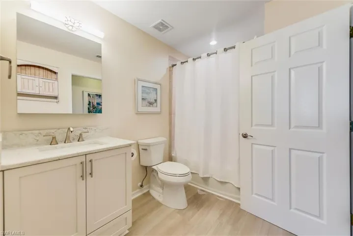 Bathroom with shower / bath combination with curtain, visible vents, toilet, vanity, and wood finished floors