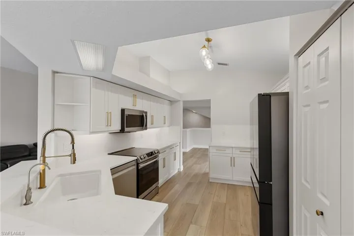 Kitchen with kitchen peninsula, appliances with stainless steel finishes, sink, light hardwood / wood-style floors, and white cabinetry