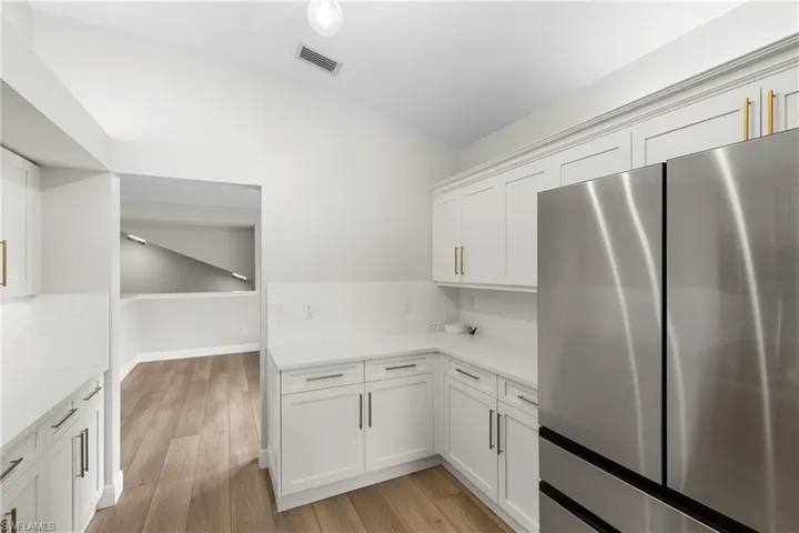 Kitchen featuring lofted ceiling, stainless steel fridge, white cabinetry, and light hardwood / wood-style flooring