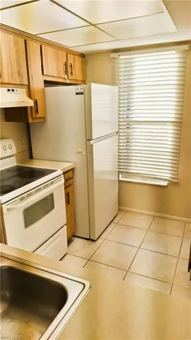 Kitchen featuring white range with electric stovetop, brown cabinetry, under cabinet range hood, light countertops, and light tile patterned floors