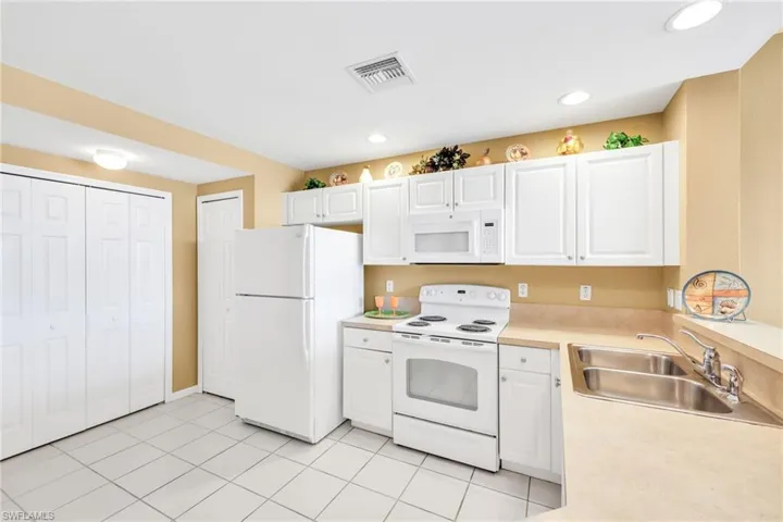 Kitchen featuring white appliances, light countertops, white cabinetry, light tile patterned floors, and recessed lighting