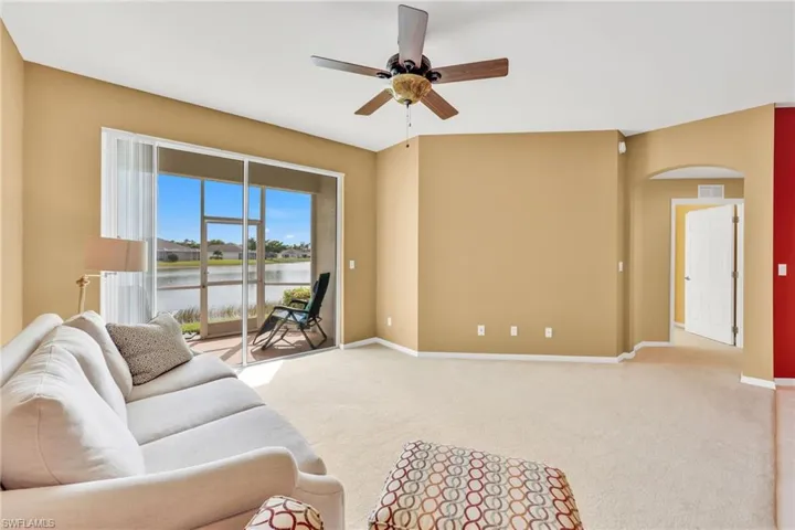 Carpeted living room featuring a water view, arched walkways, and a ceiling fan